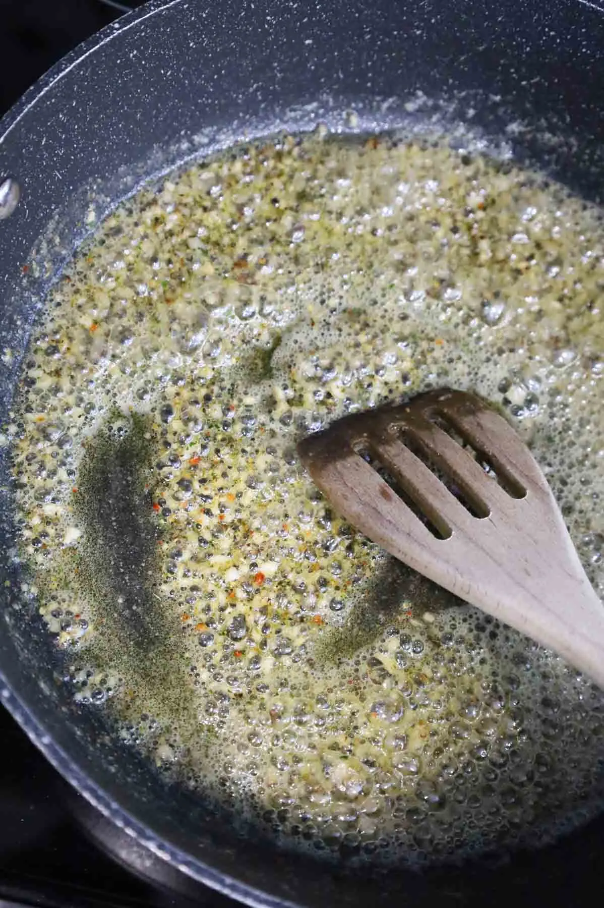 minced garlic and Italian seasoning being stirred with melted butter