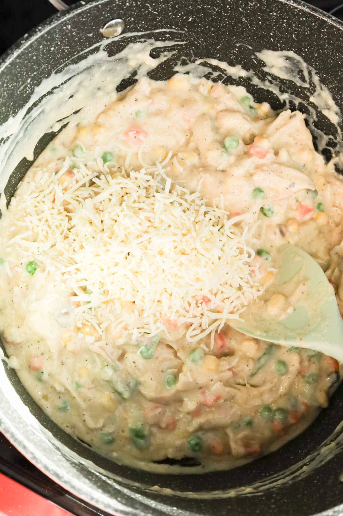 shredded parmesan cheese added to pot with creamy chicken and vegetable mixture in a pot