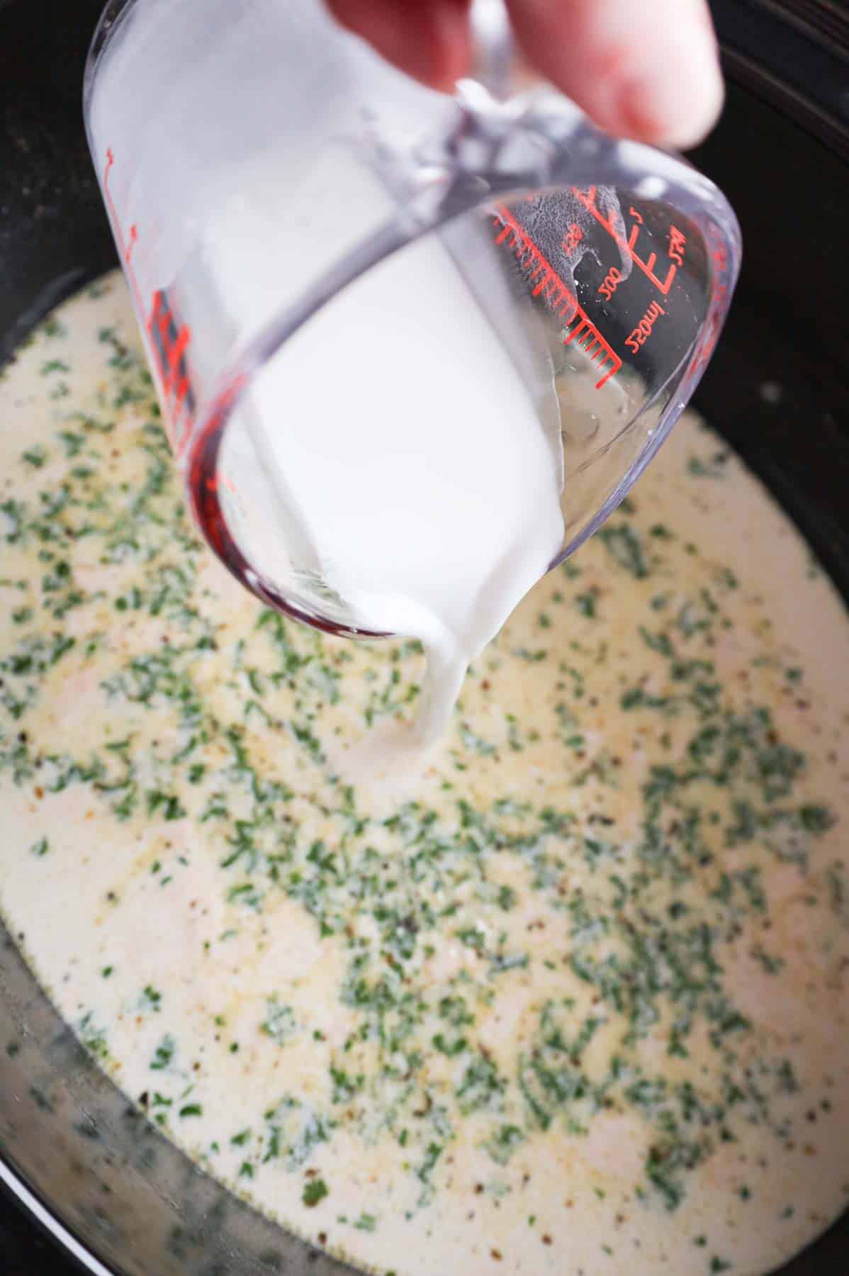 cornstarch slurry being poured into crock pot with creamy garlic parmesan sauce