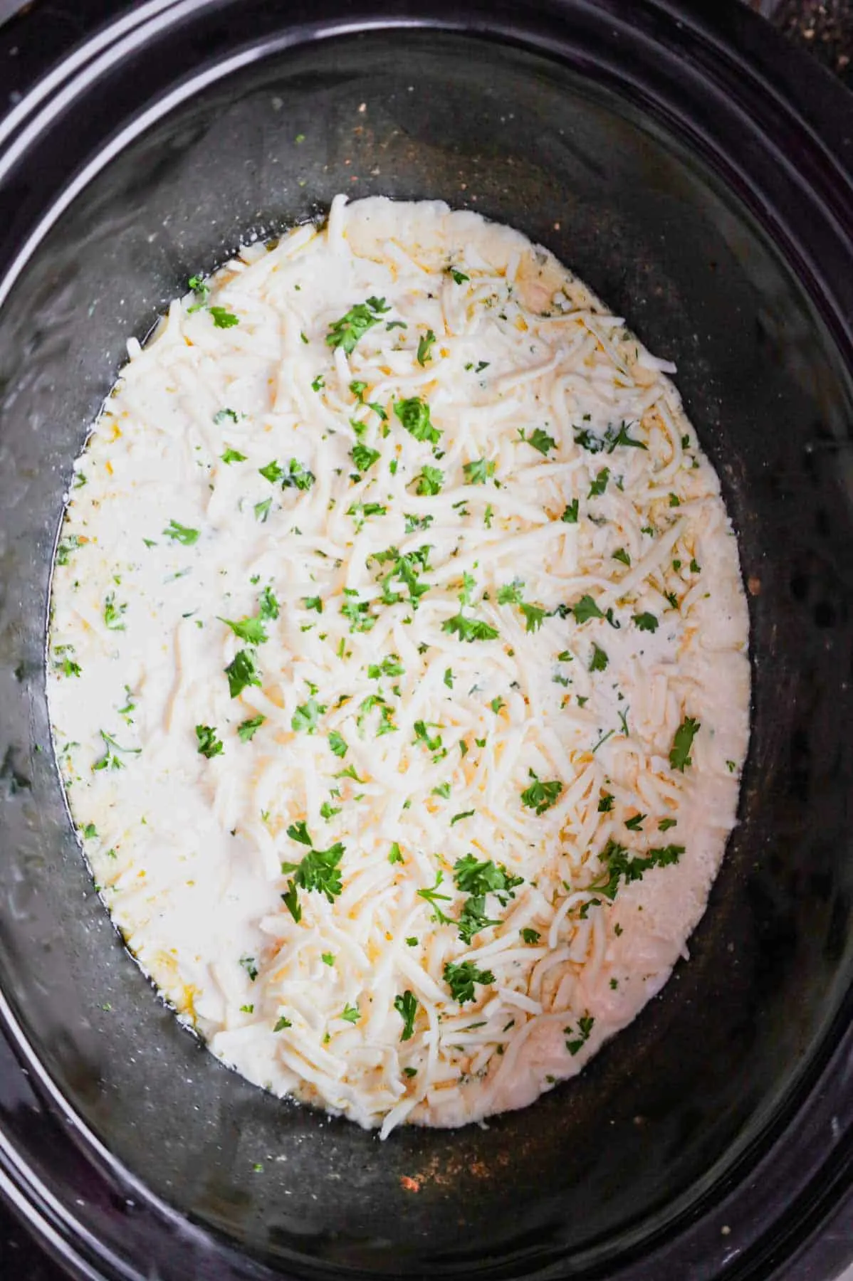 shredded mozzarella and chopped parsley on top of parmesan garlic chicken breasts in a crock pot