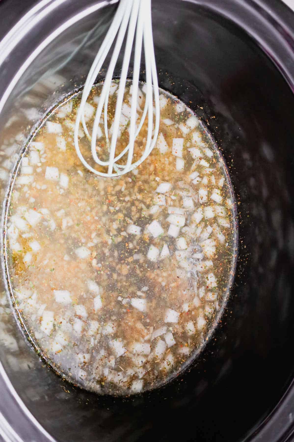 whisking chicken broth, diced onions, minced garlic and Italian seasoning in a slow cooker