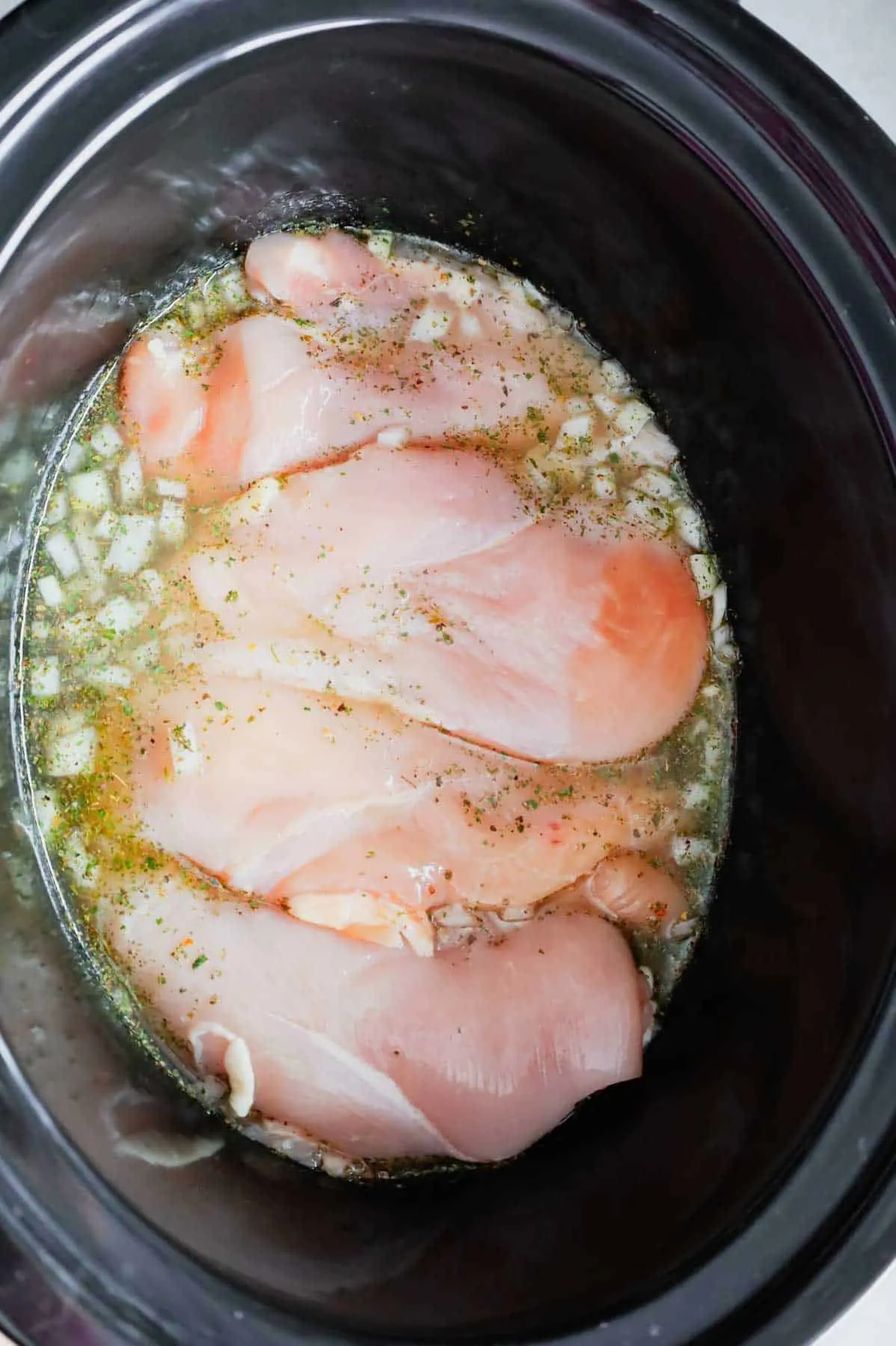 chicken breasts and diced onions in chicken broth in a slow cooker