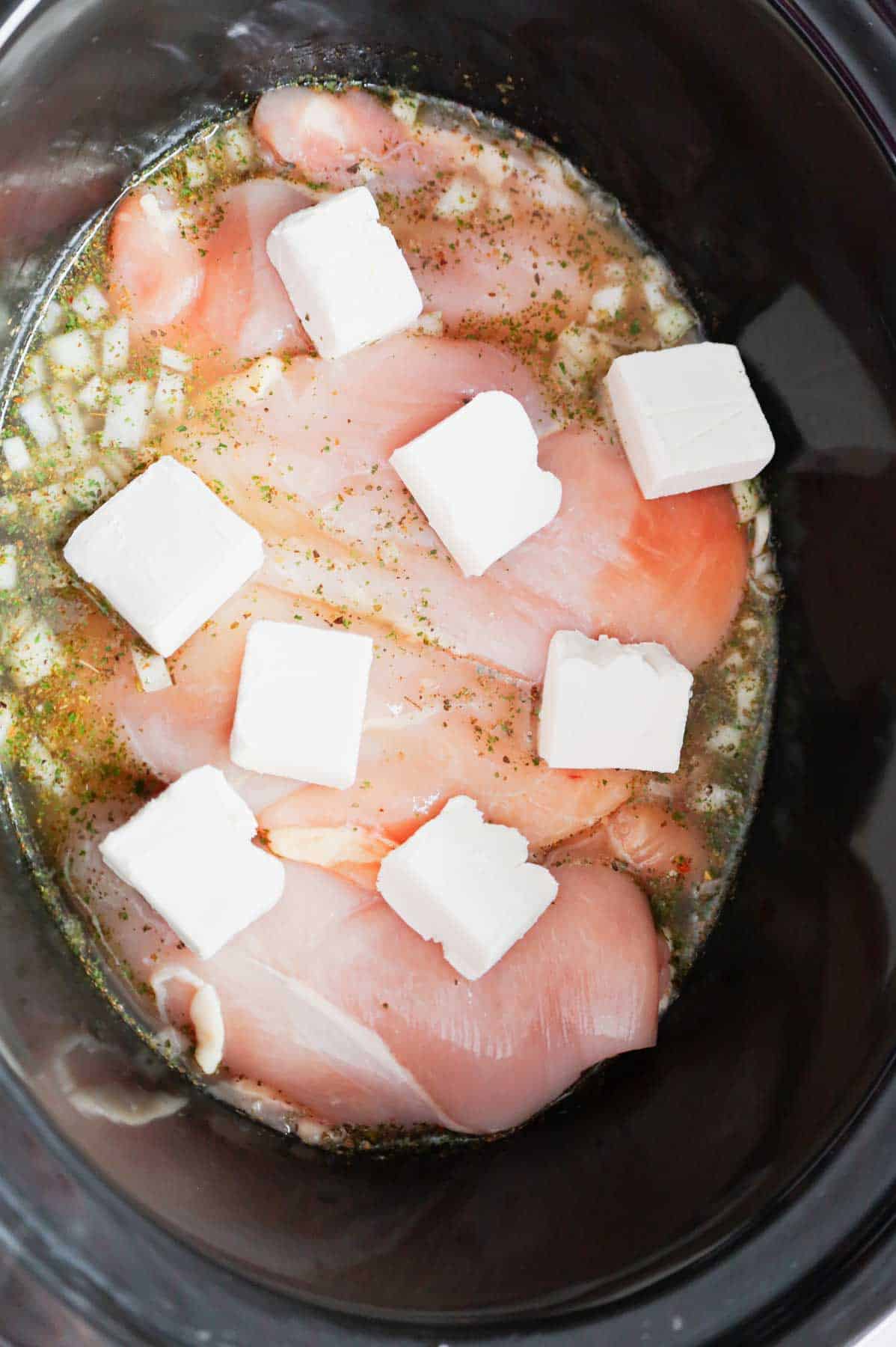 cream cheese cubes on top of chicken breasts in a crock pot