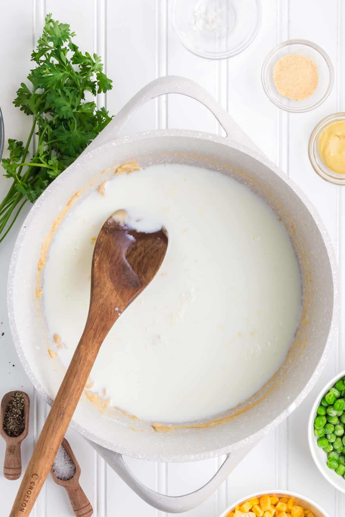 milk and roux being stirred together in a pot