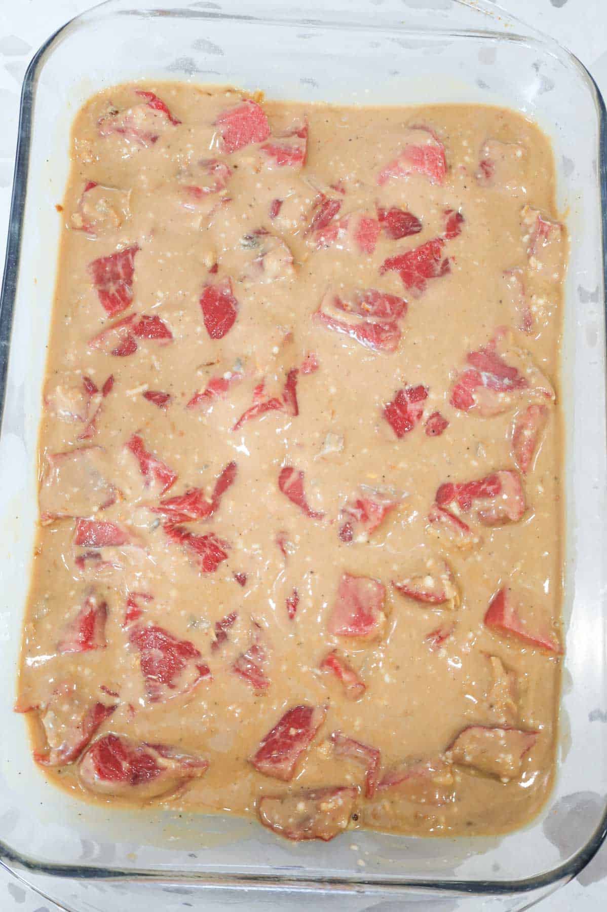 cream of mushroom soup and gravy soup mixture in a baking dish with beef cubes
