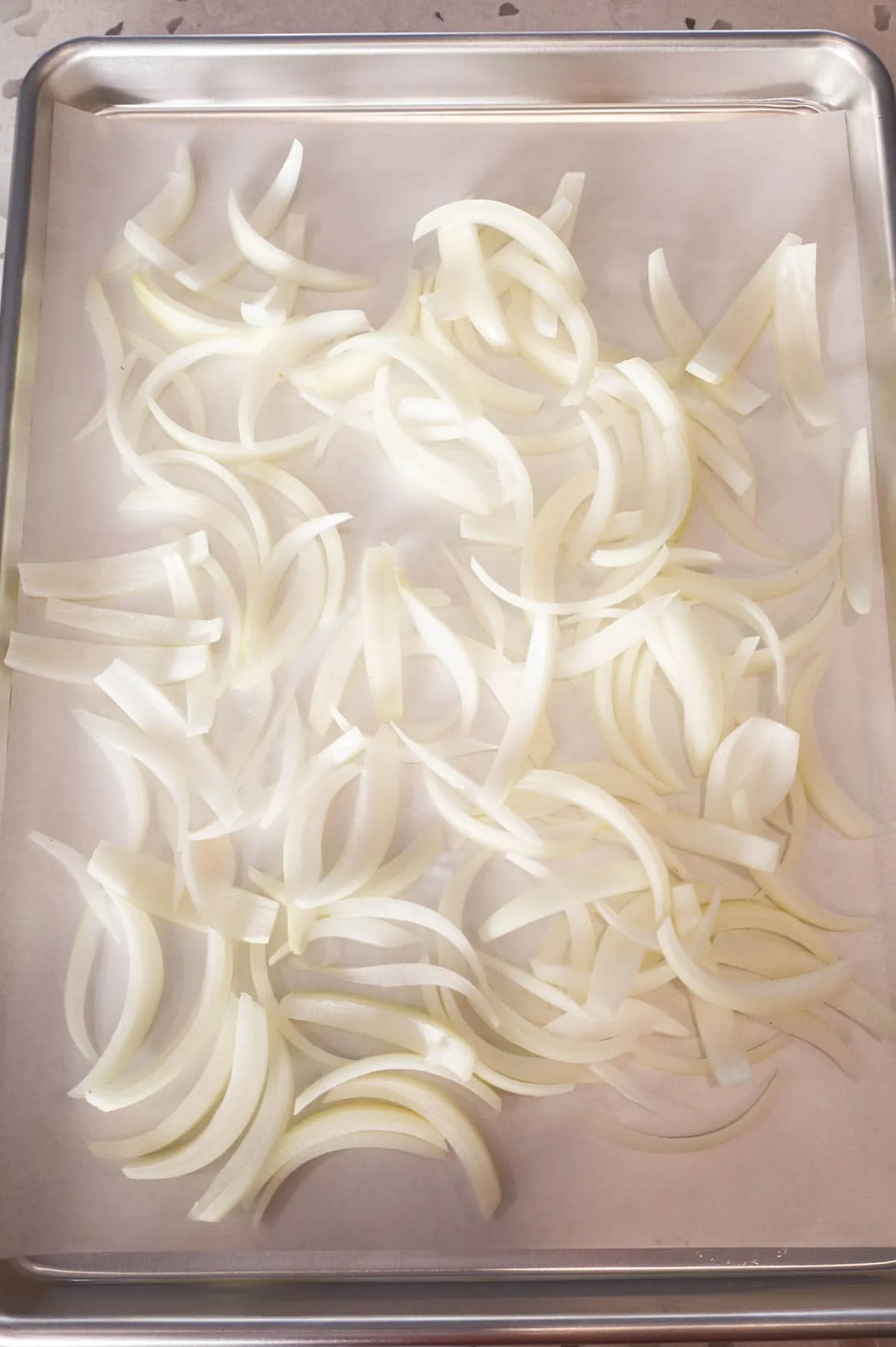 sliced onions on a parchment lined sheet pan