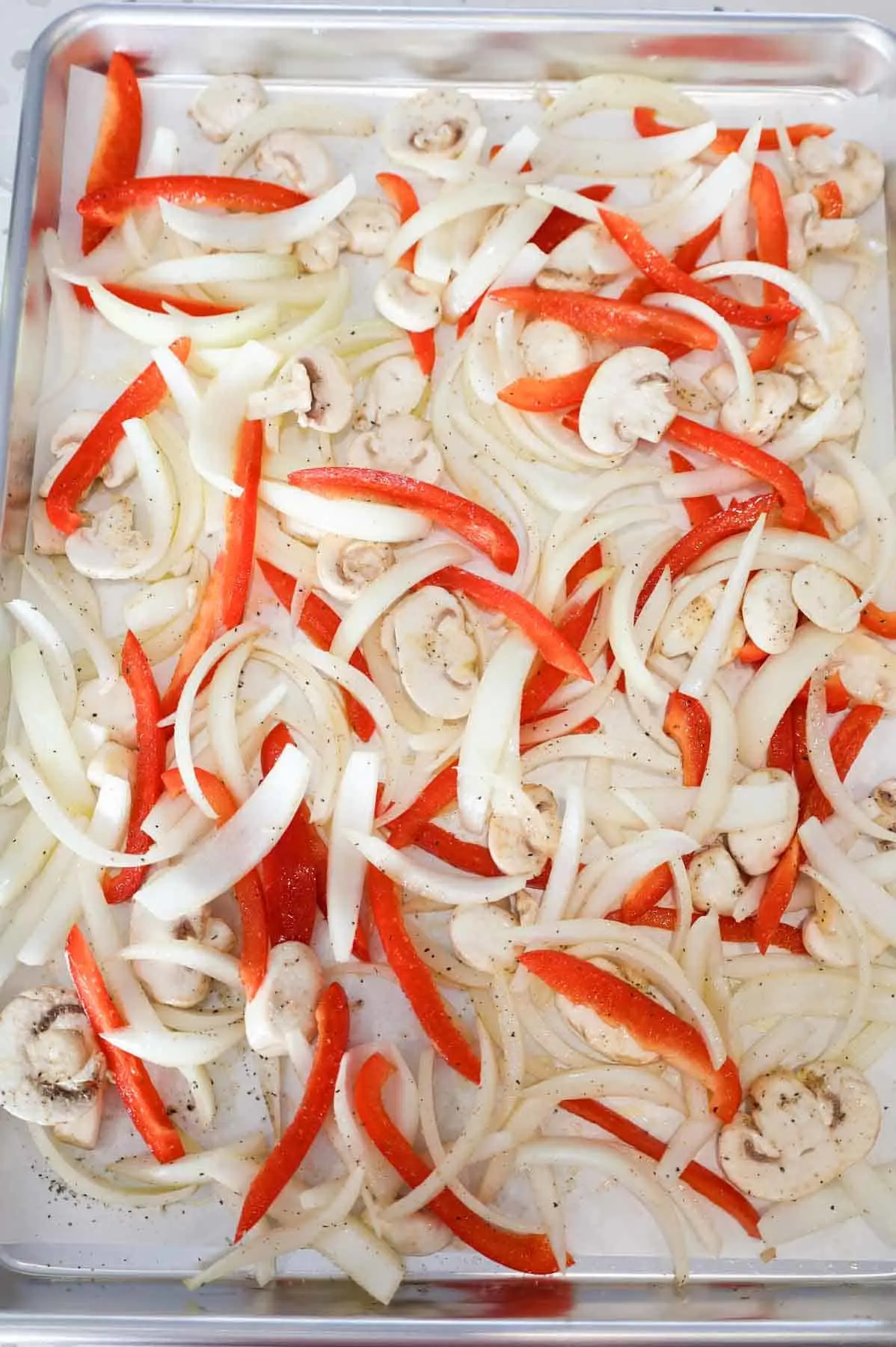 seasoned sliced mushrooms, red bell peppers and onions on a parchment lined baking sheet