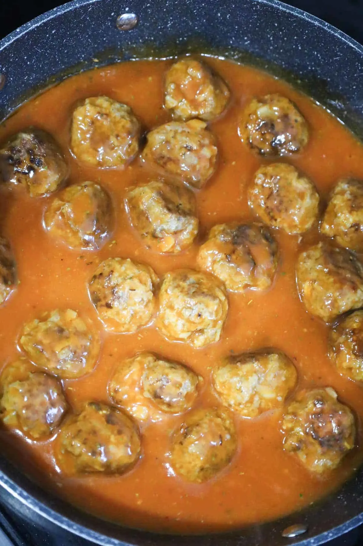 browned meatballs covered in tomato soup sauce in a skillet