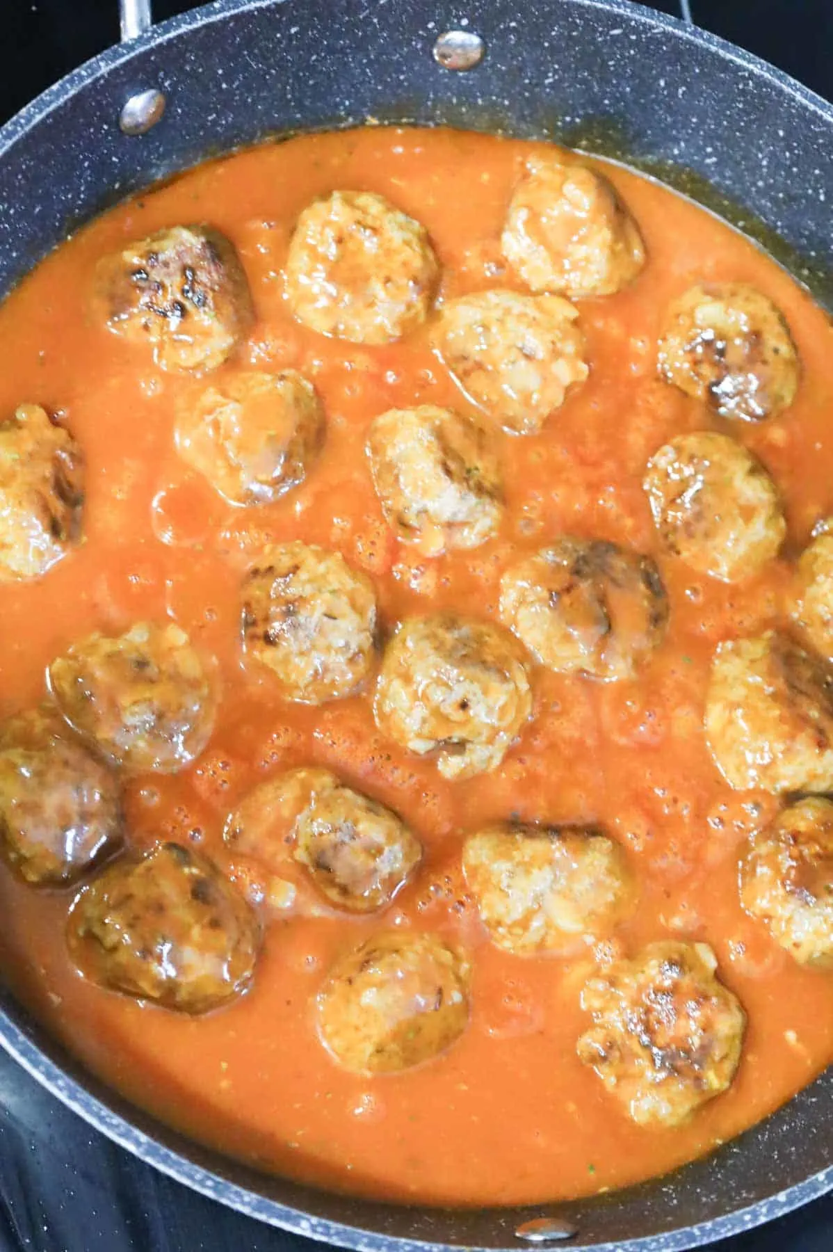browned meatballs simmering in tomato soup sauce