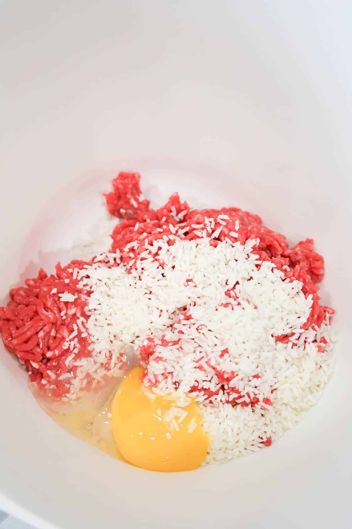 minute rice and an egg on top of raw ground beef in a bowl