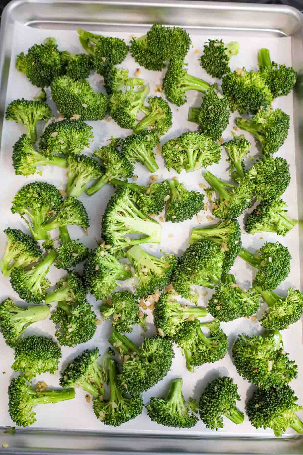 broccoli florets tossed in seasoning and olive oil on a parchment lined baking sheet