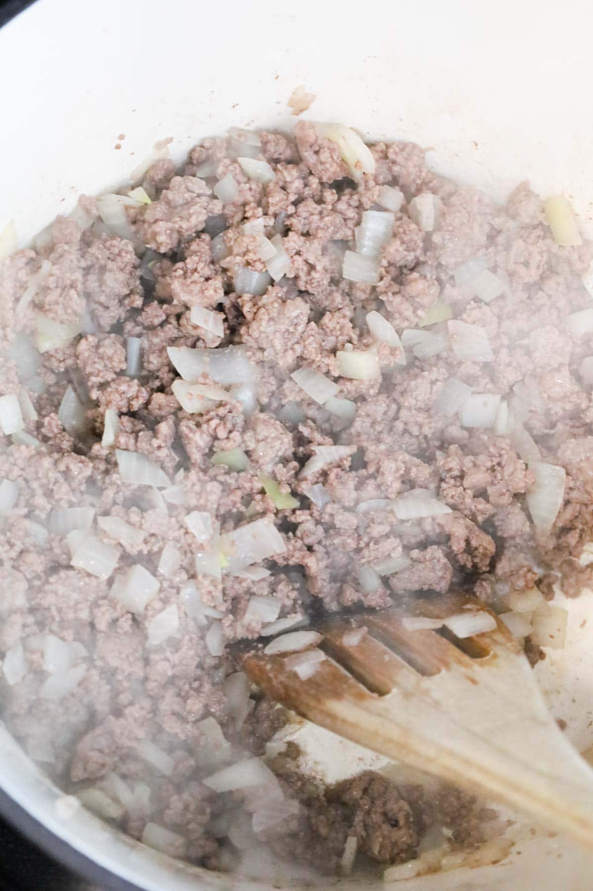 ground beef and diced onions being stirred in a Dutch oven