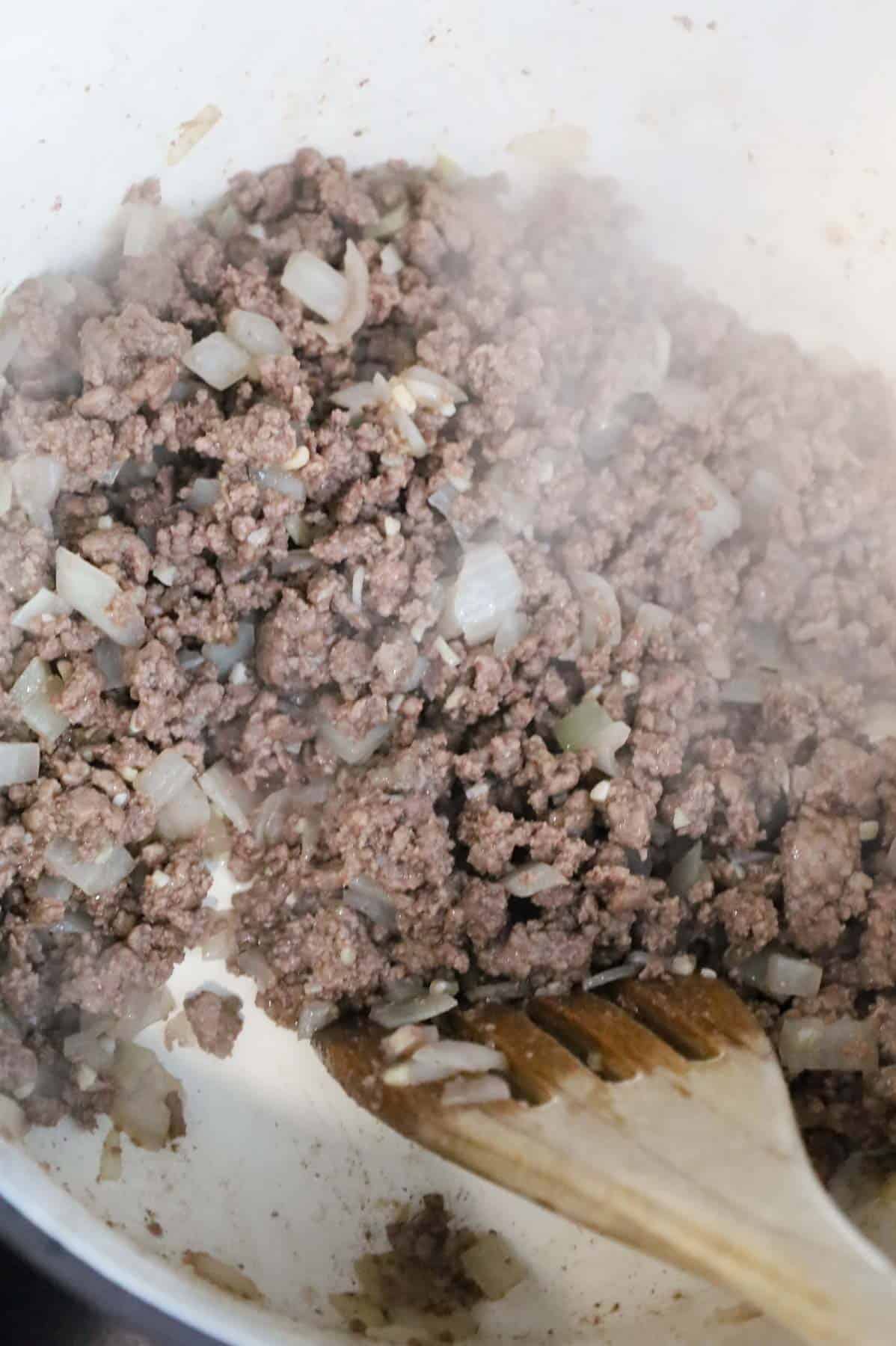 minced garlic being stirred with cooked ground beef and diced onions