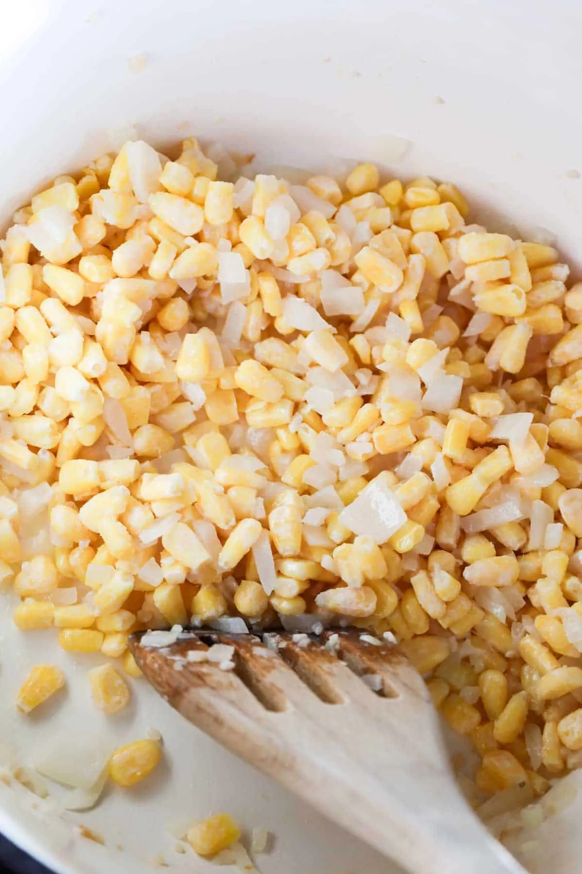 frozen corn and diced onions being stirred in a pot