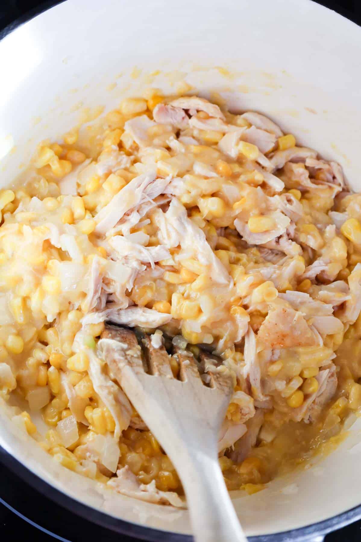 shredded chicken and creamed corn being stirred in a pot