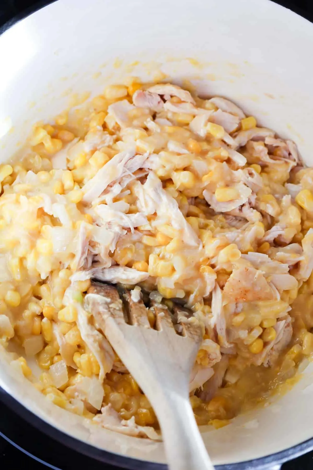 shredded chicken and creamed corn being stirred in a pot