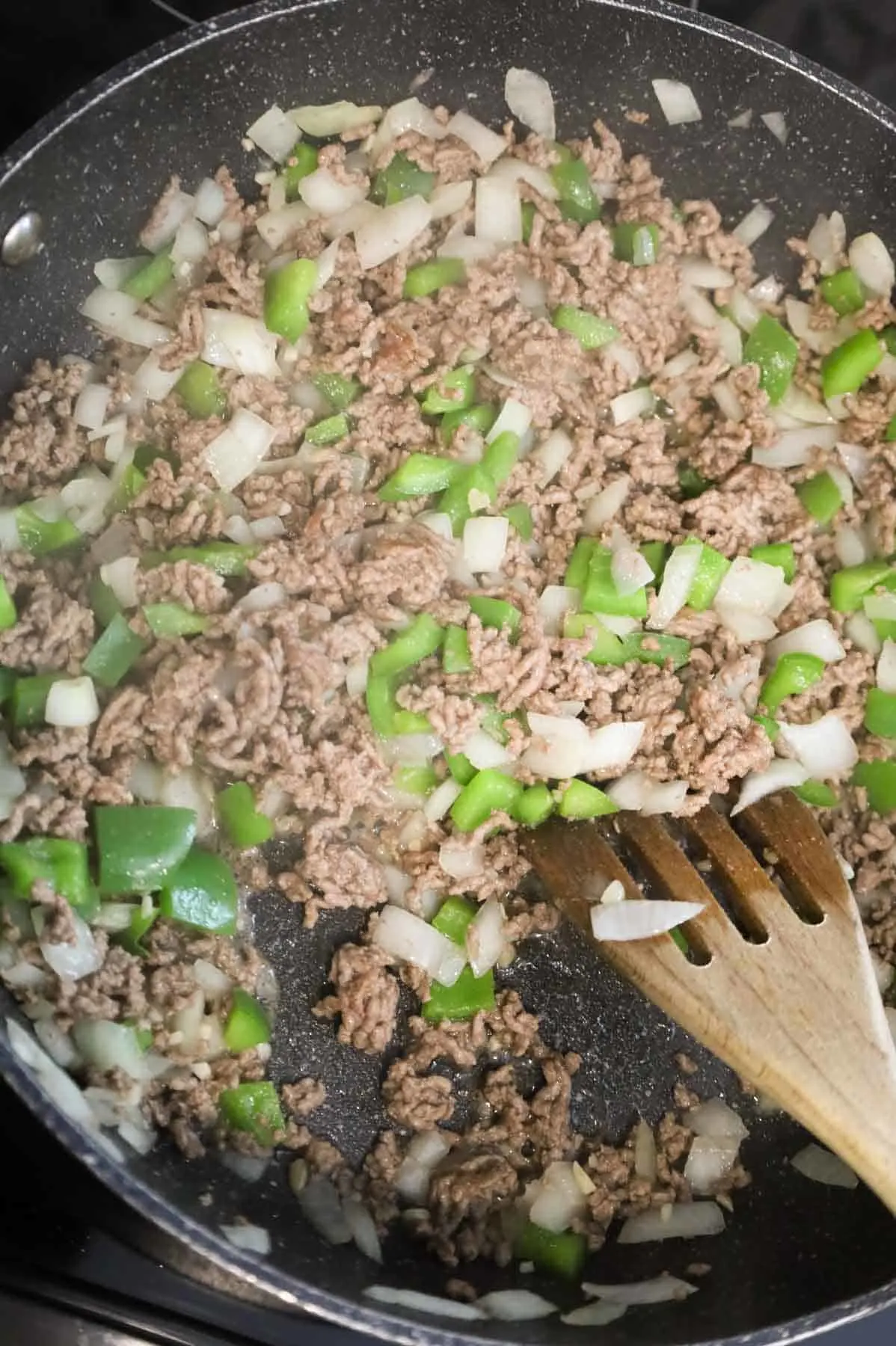 ground beef, diced onions and green peppers being stirred in a skillet