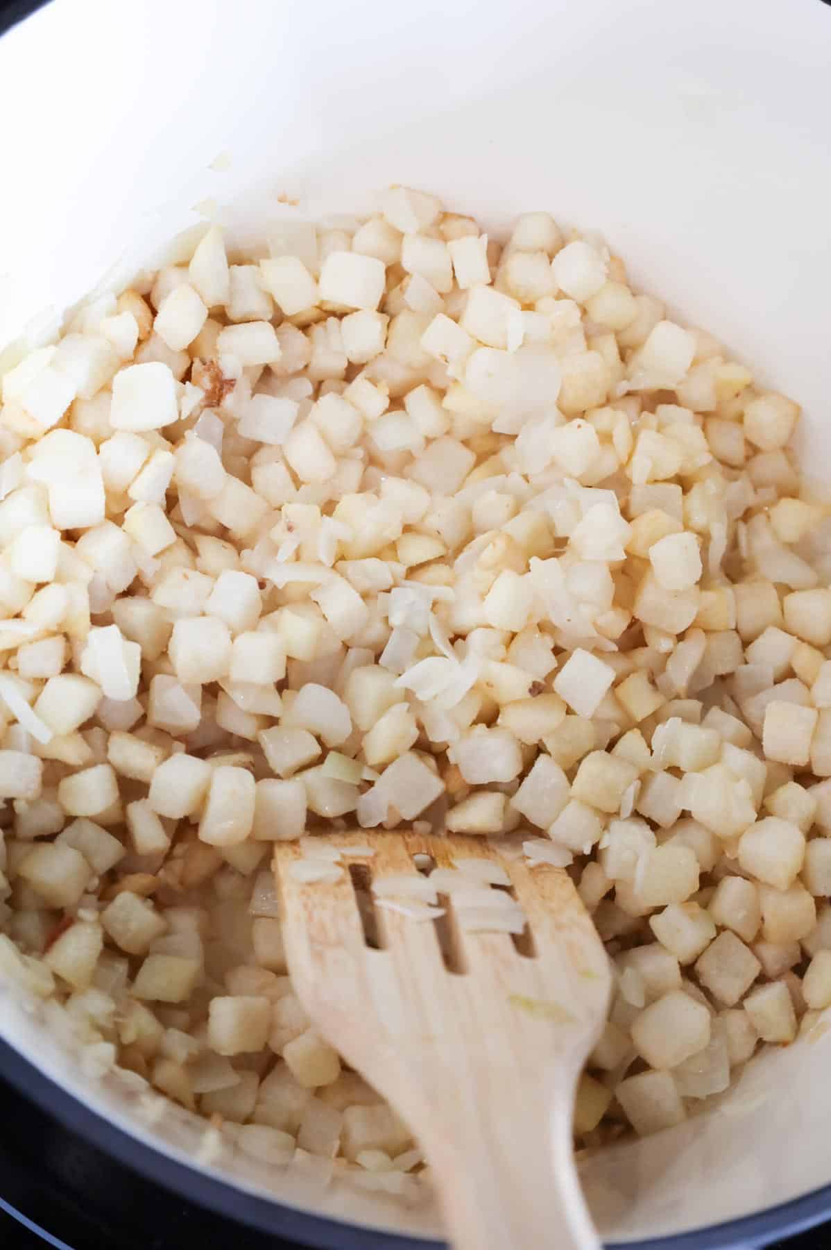 diced hash brown potatoes being stirred with diced onions in a pot