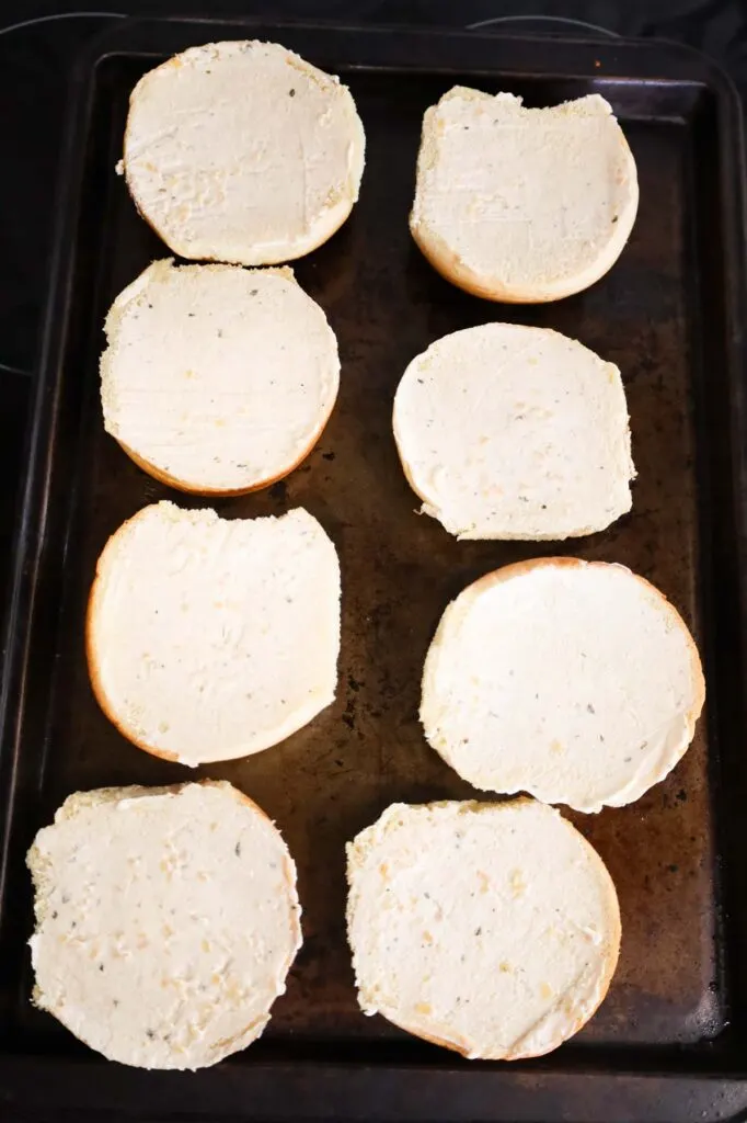 hamburger buns spread with garlic butter on a baking sheet