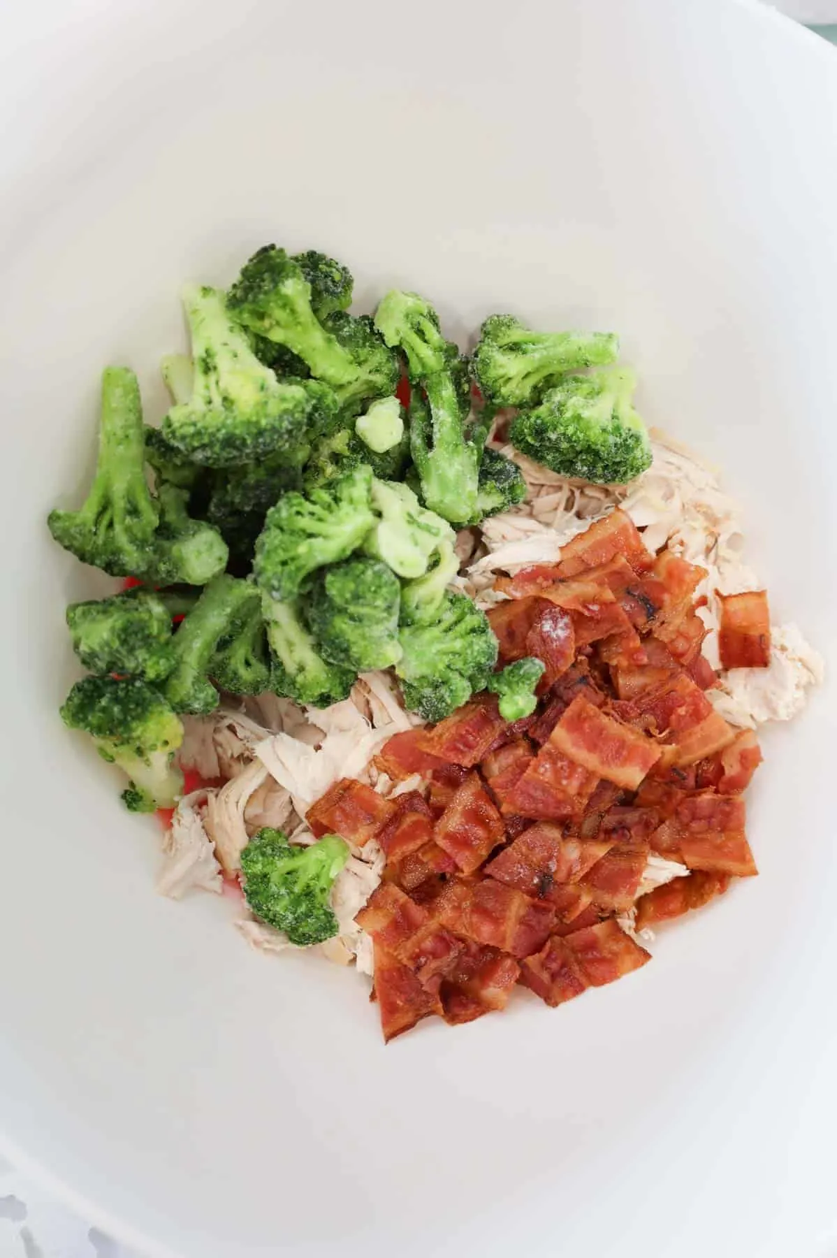 broccoli, shredded chicken and bacon pieces in a mixing bowl