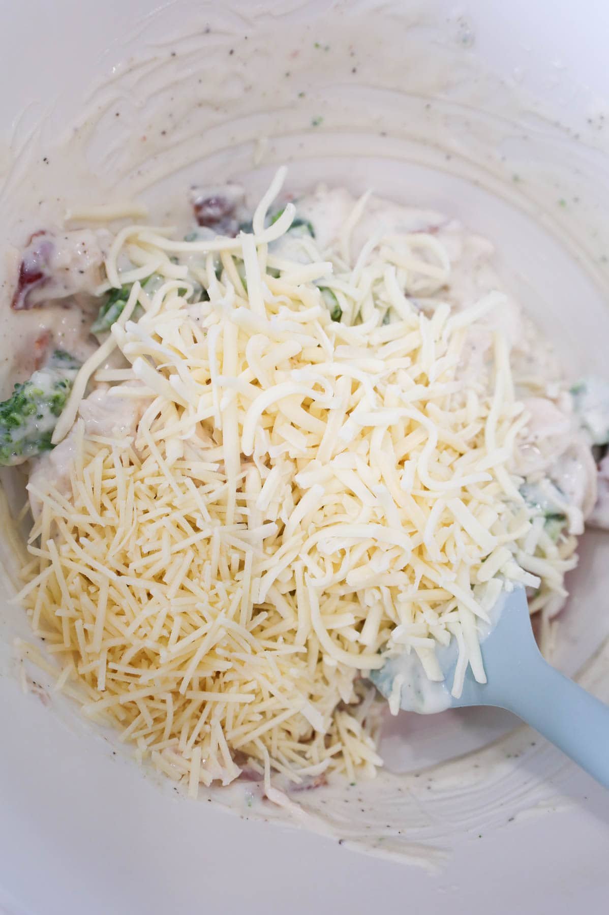 shredded mozzarella and shredded parmesan on top of a creamy chicken mixture in a mixing bowl