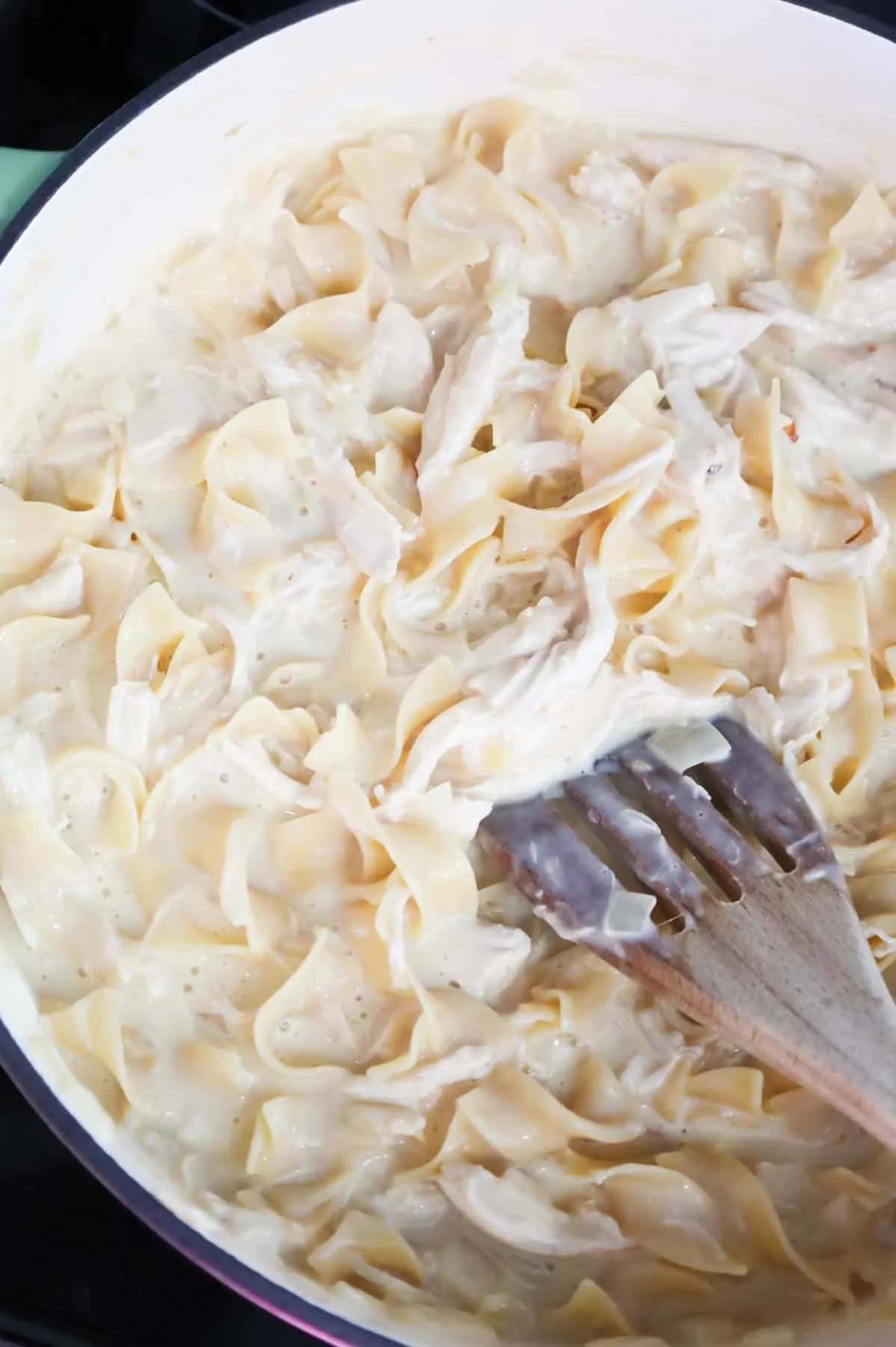 stirring chicken and egg noodles in a creamy sauce in a skillet