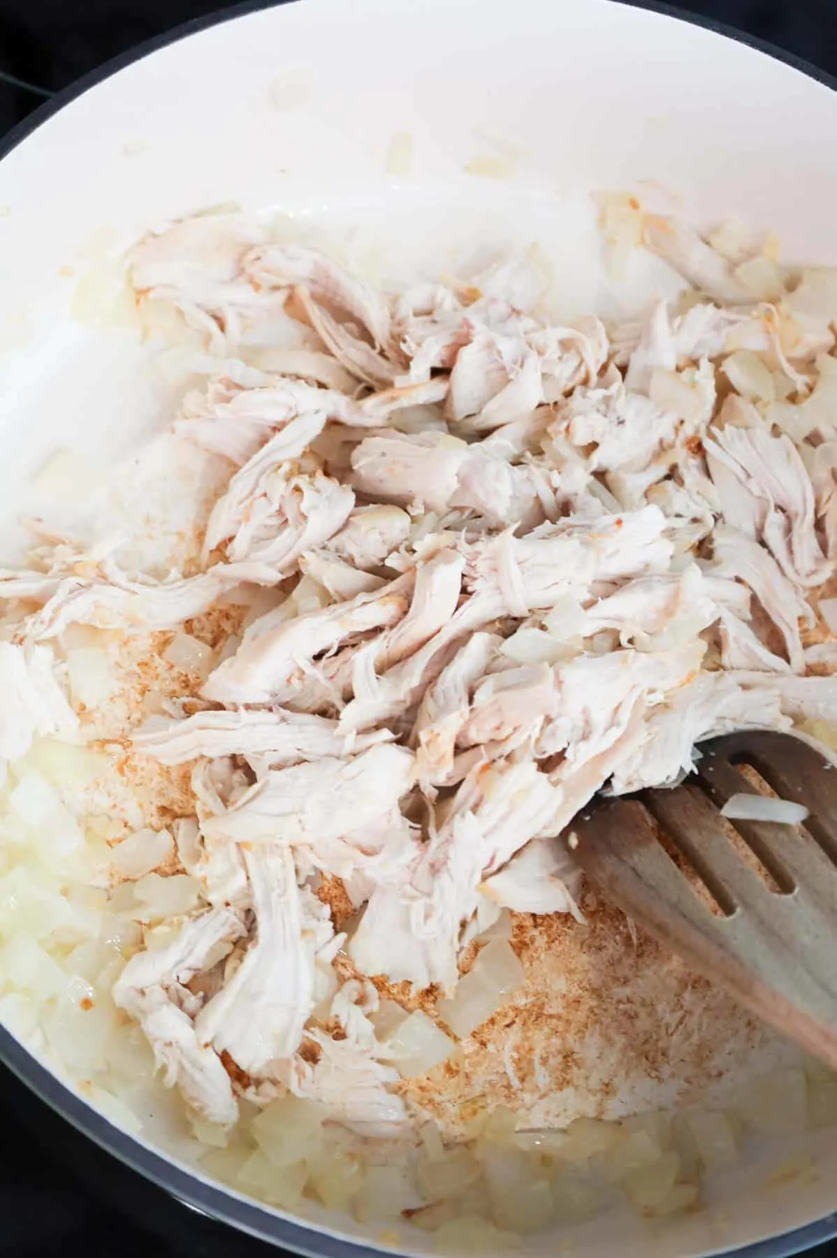 shredded chicken being stirred with diced onions in a skillet