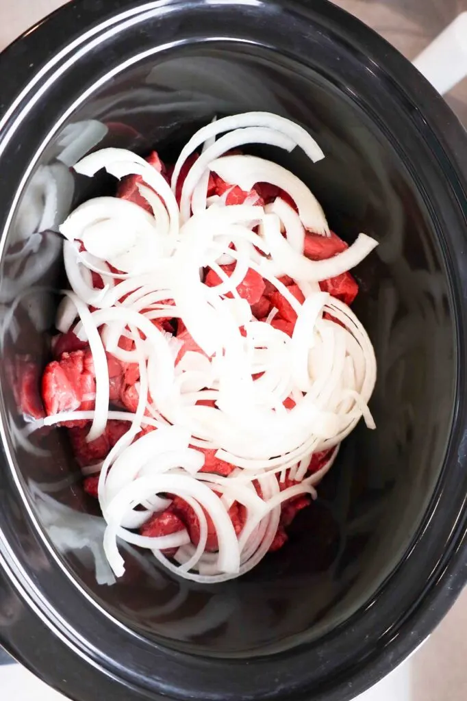 sliced onions on top of stewing beef in a Crock Pot