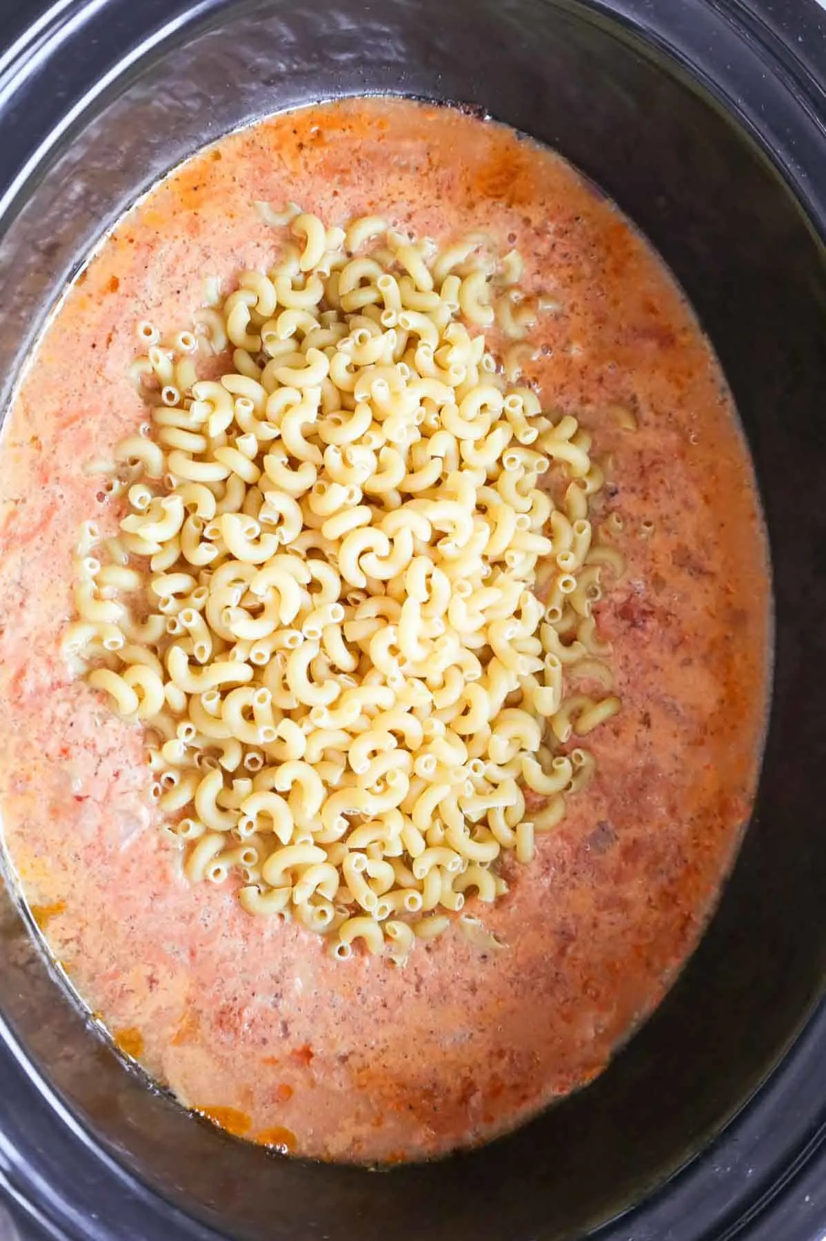 uncooked macaroni noodles added to crock pot with ground beef and sauce mixture