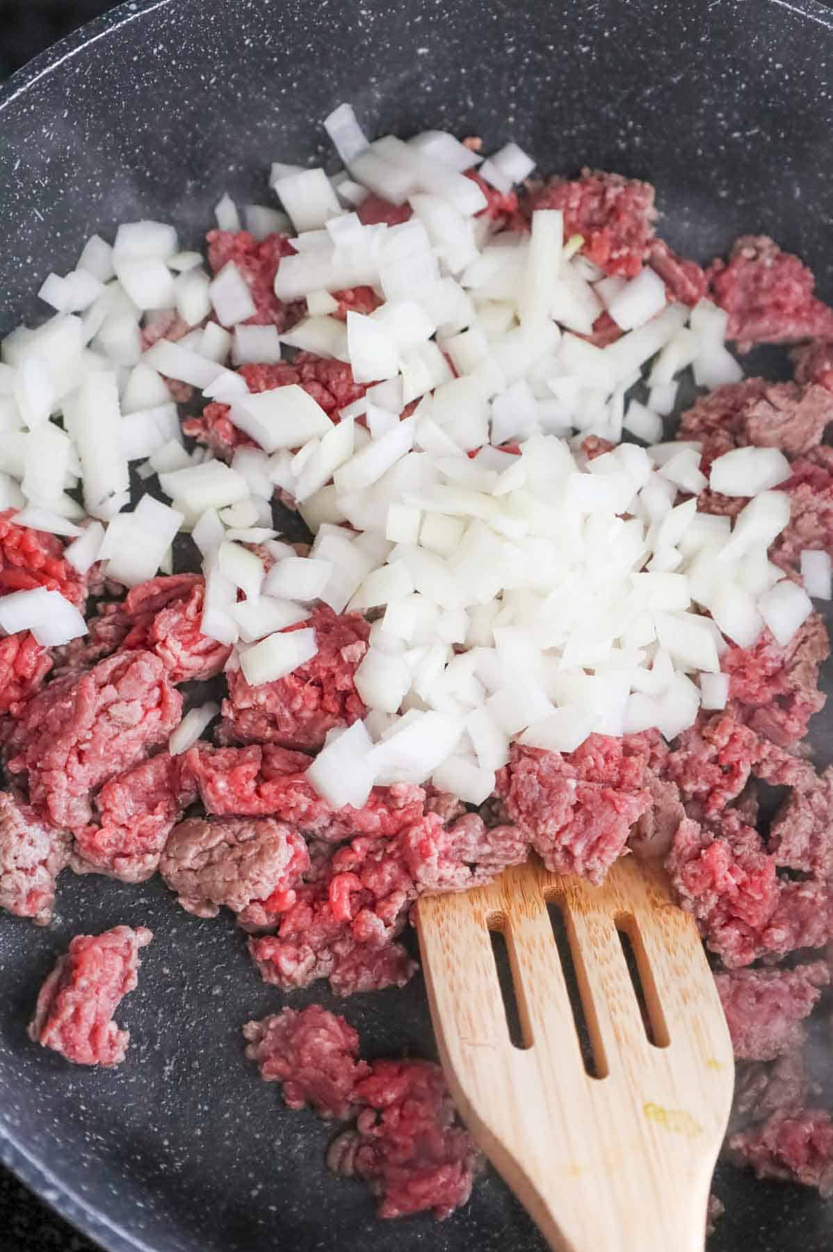 diced onions on top of ground beef in a skillet