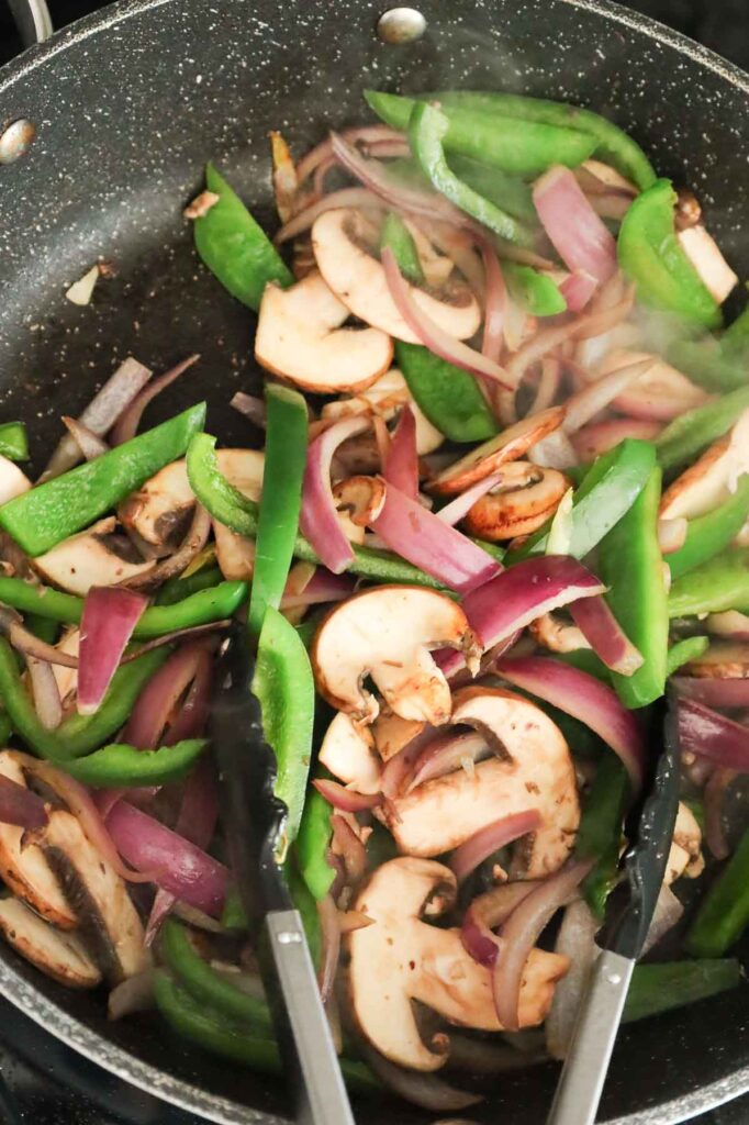 stirring sliced mushrooms, green peppers and red onions in a skillet