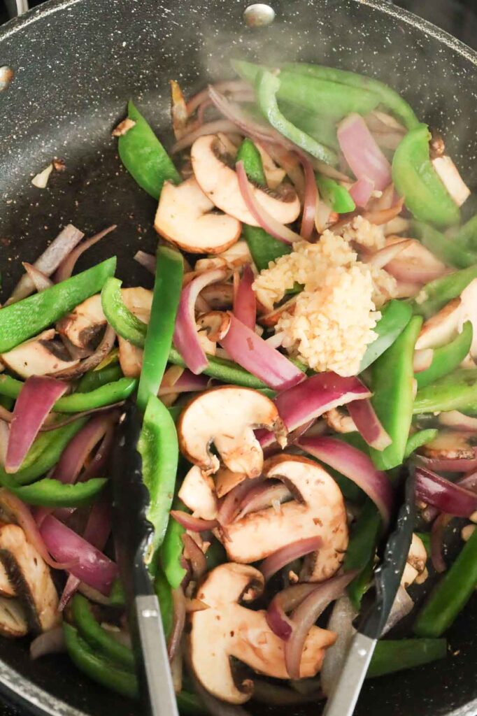 minced garlic on top of sliced mushrooms, green peppers and red onions in a skillet