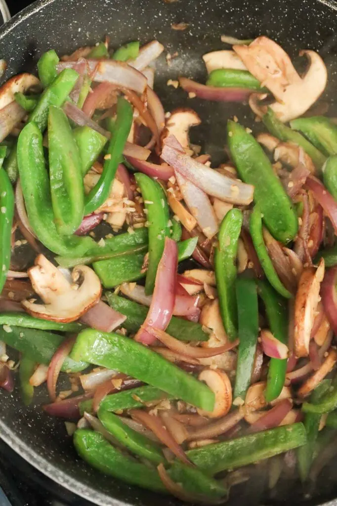green peppers, red onions and sliced mushrooms cooking in a skillet