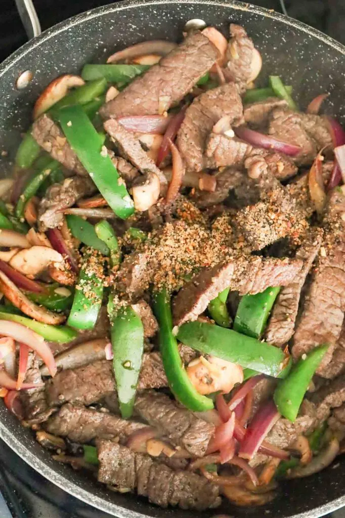 steak spice on top of steak strips, sliced green peppers, red onions and mushrooms in a skillet