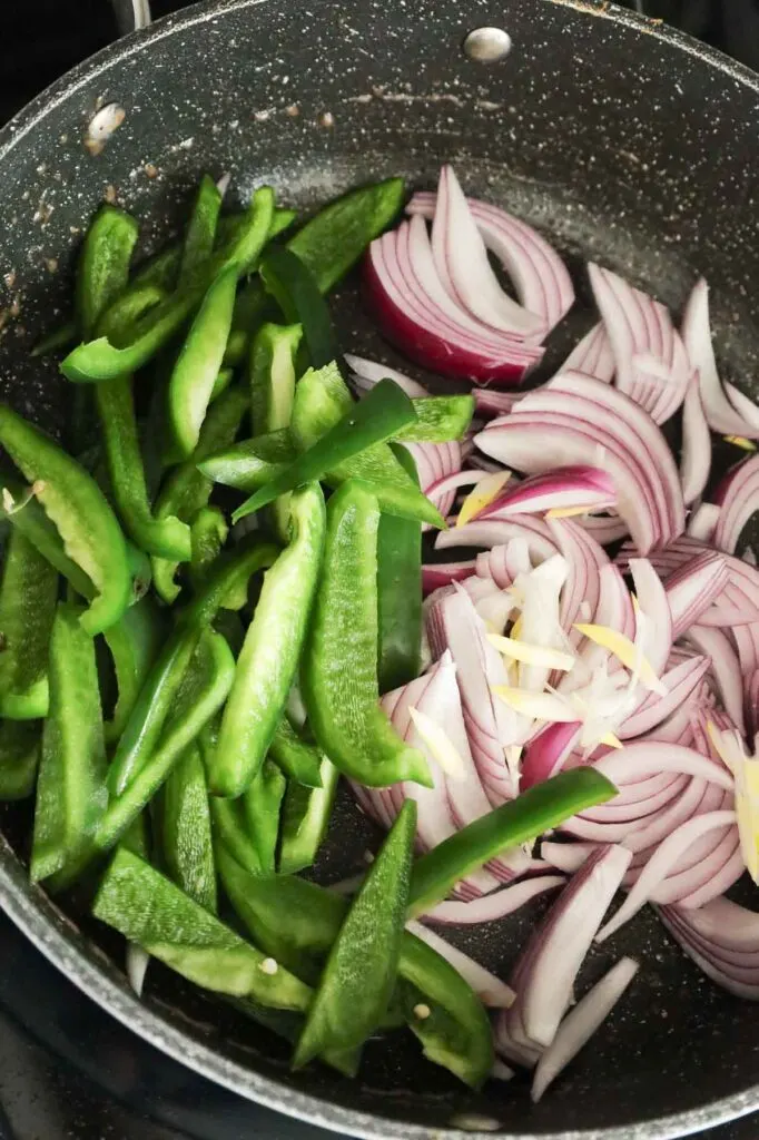 sliced green peppers and red onions added to a hot skillet