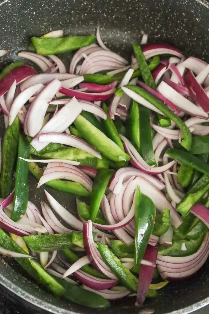 sliced red onions and green peppers cooking in a skillet