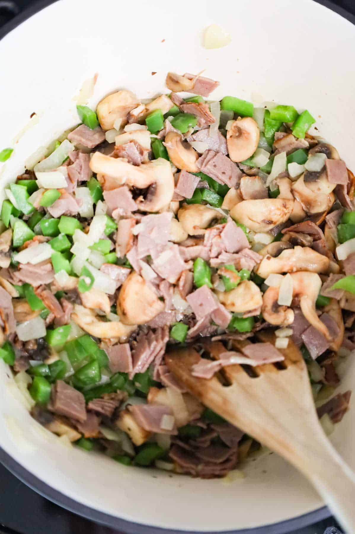 stirring chopped roast beef in a Dutch oven with green peppers, onions and mushrooms