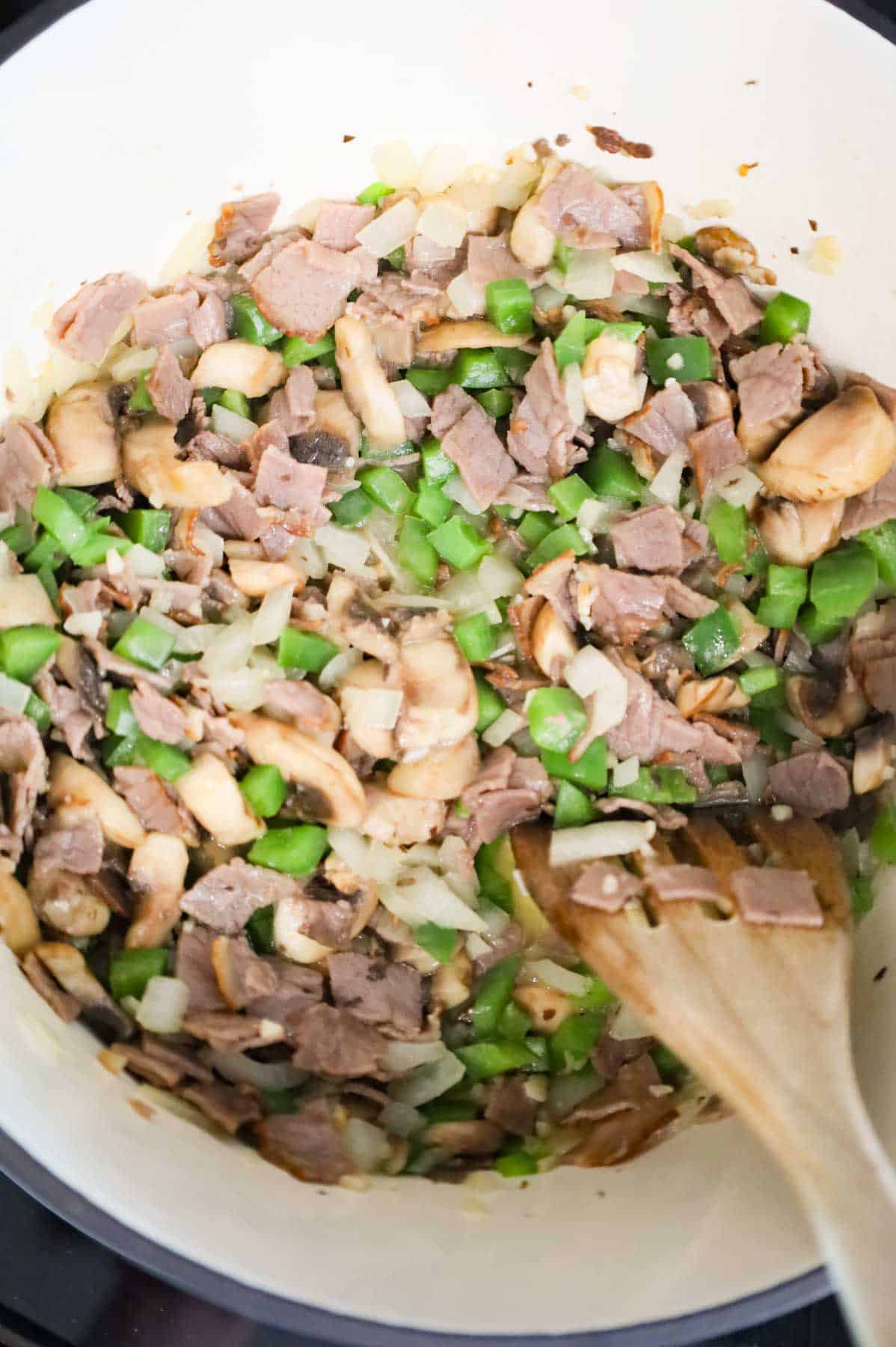 stirring minced garlic with roast beef, green peppers and onions