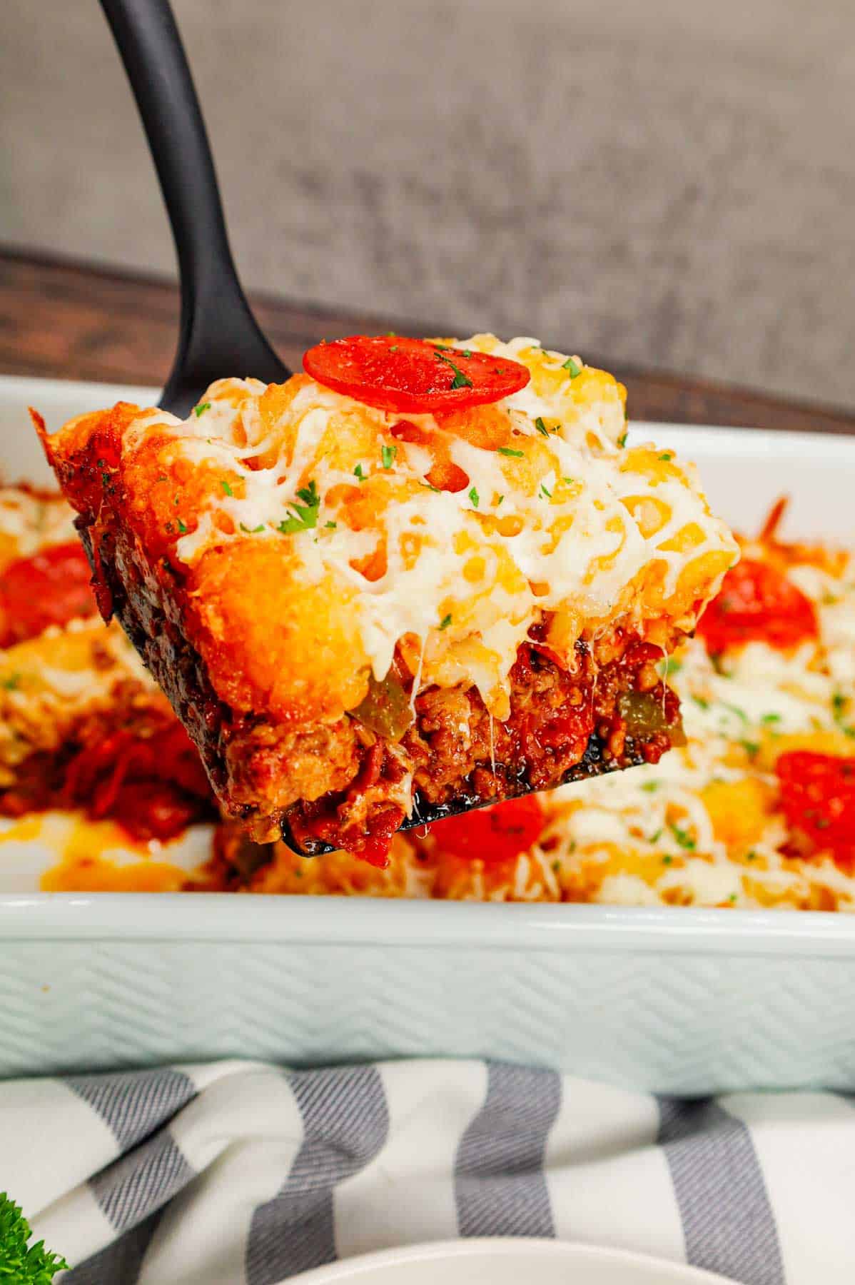 Pizza Tater Tot Casserole is a hearty casserole loaded with ground beef, Italian sausage, pepperoni, green peppers, onions, pizza sauce, mozzarella cheese and crispy tater tots.