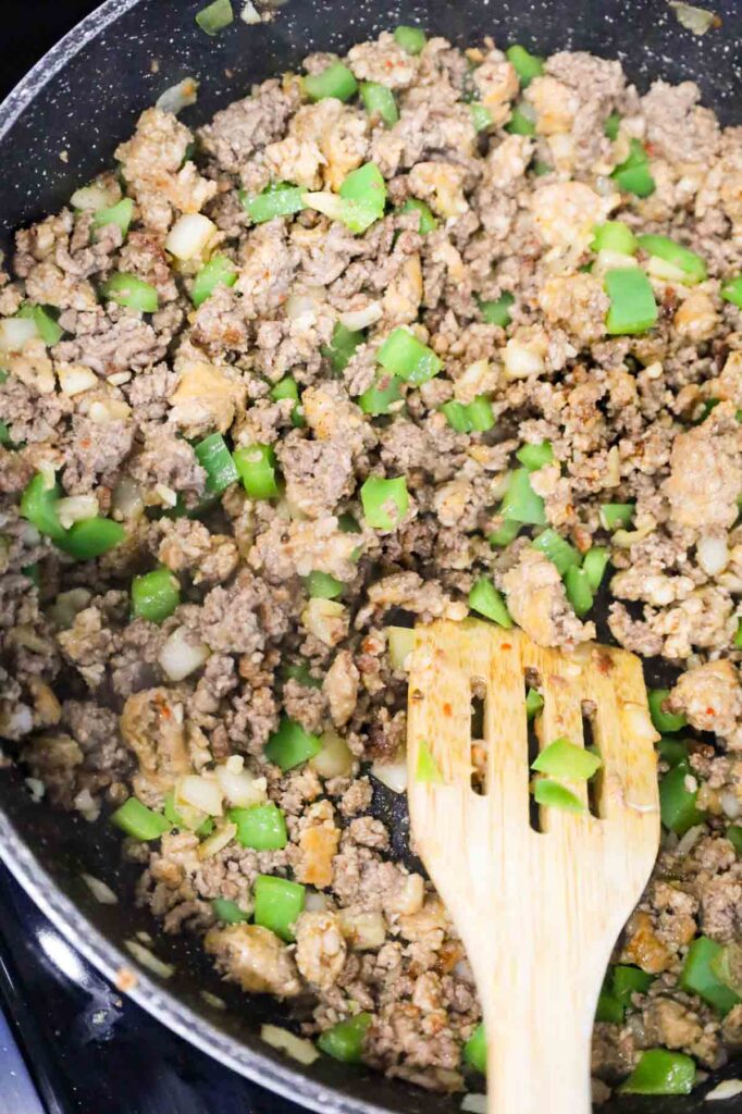 stirring garlic with ground beef, sausage meat and green peppers in a skillet