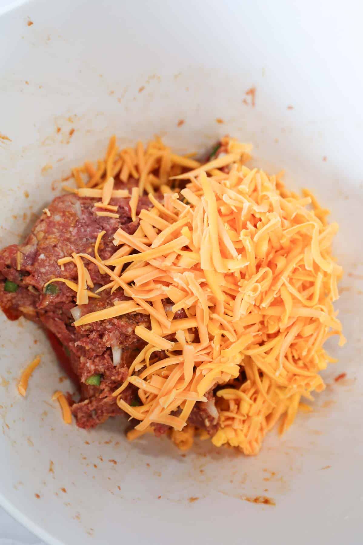shredded cheddar cheese on top of raw meatloaf mixture in a mixing bowl