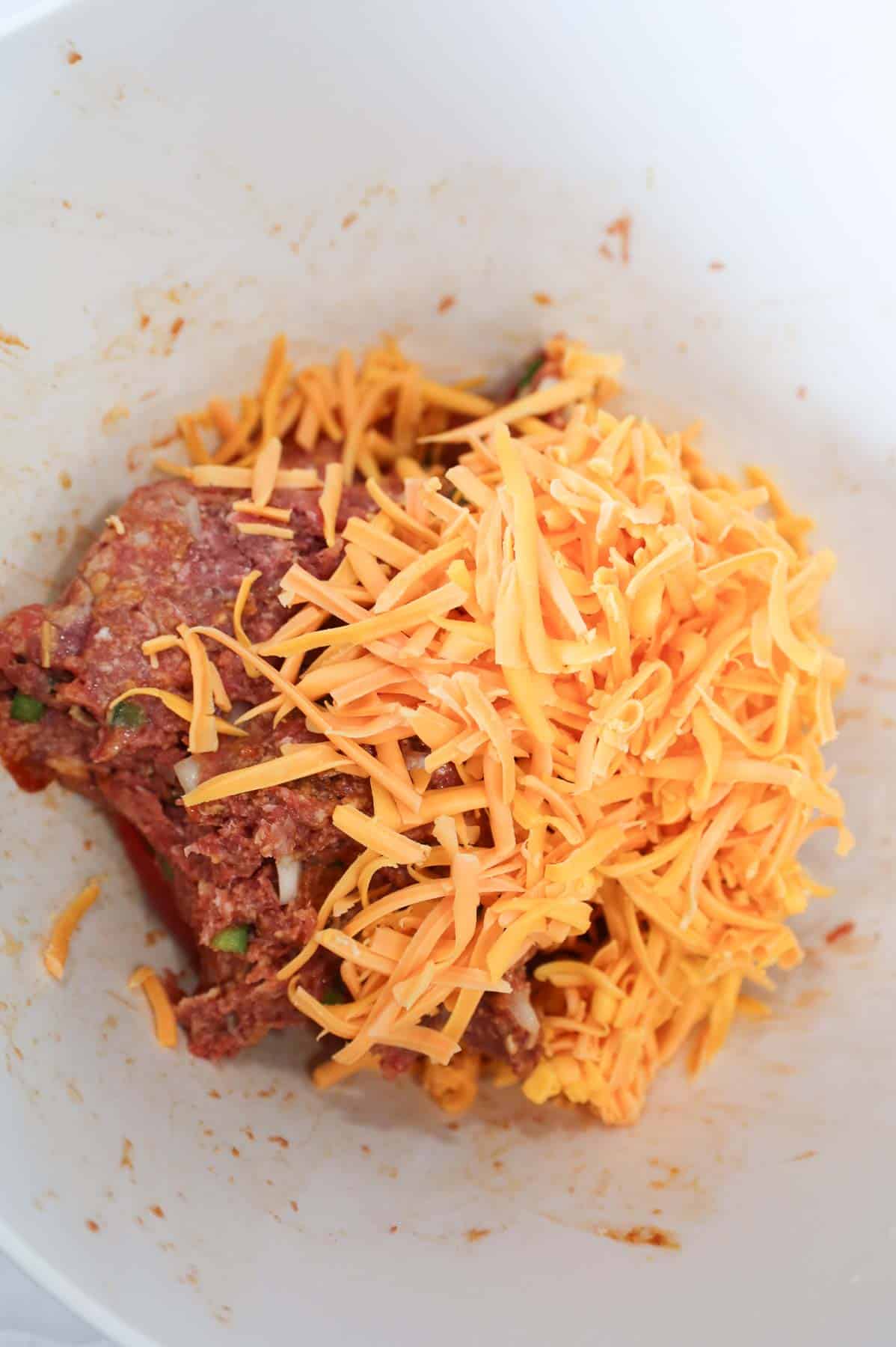 shredded cheddar cheese on top of raw meatloaf mixture in a mixing bowl