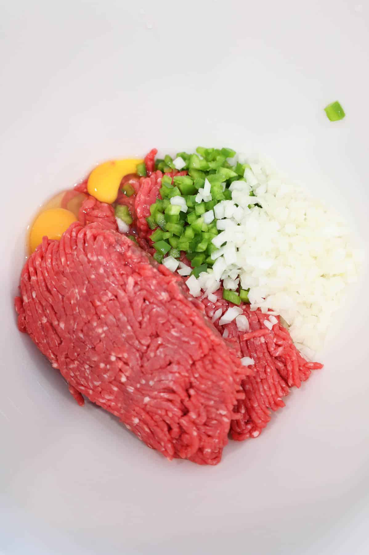 diced onions, green peppers, eggs and ground beef in a mixing bowl