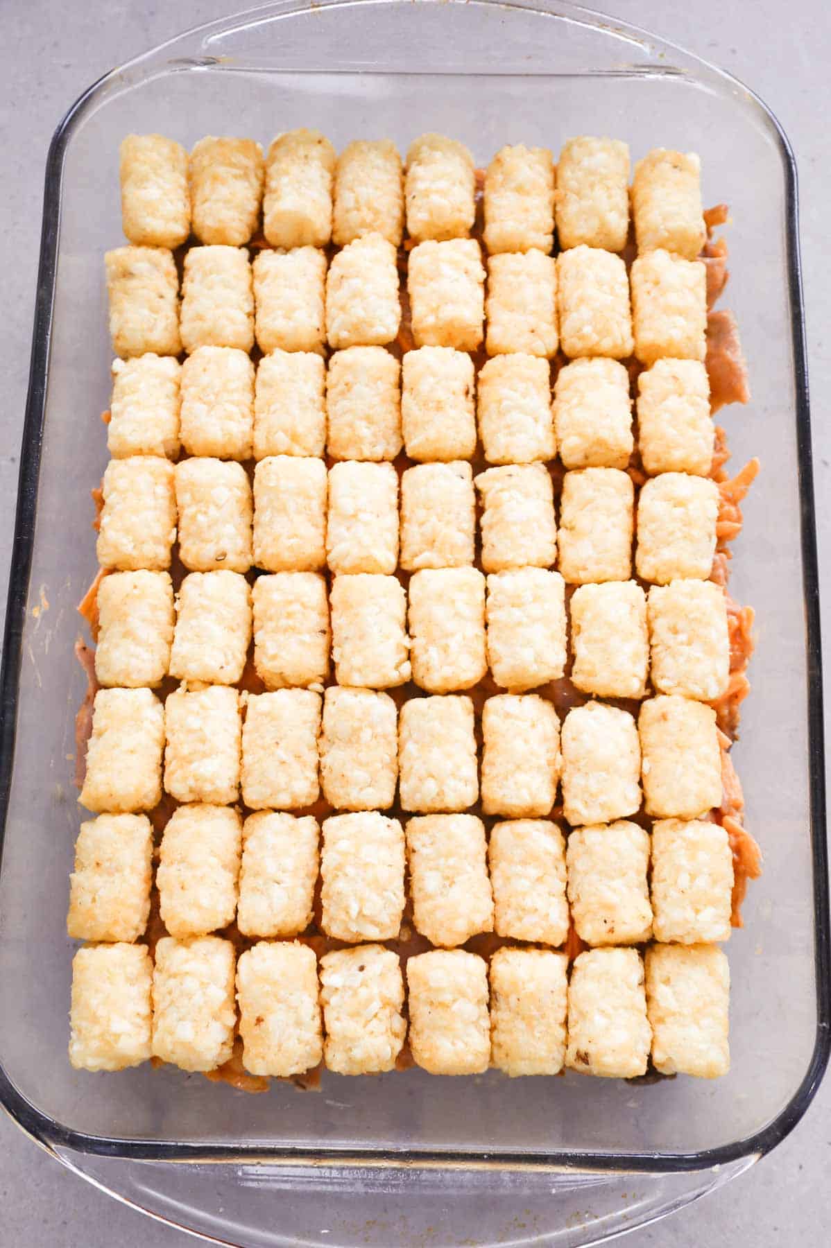 frozen tater tots on top of roast beef and cheddar mixture in casserole dish