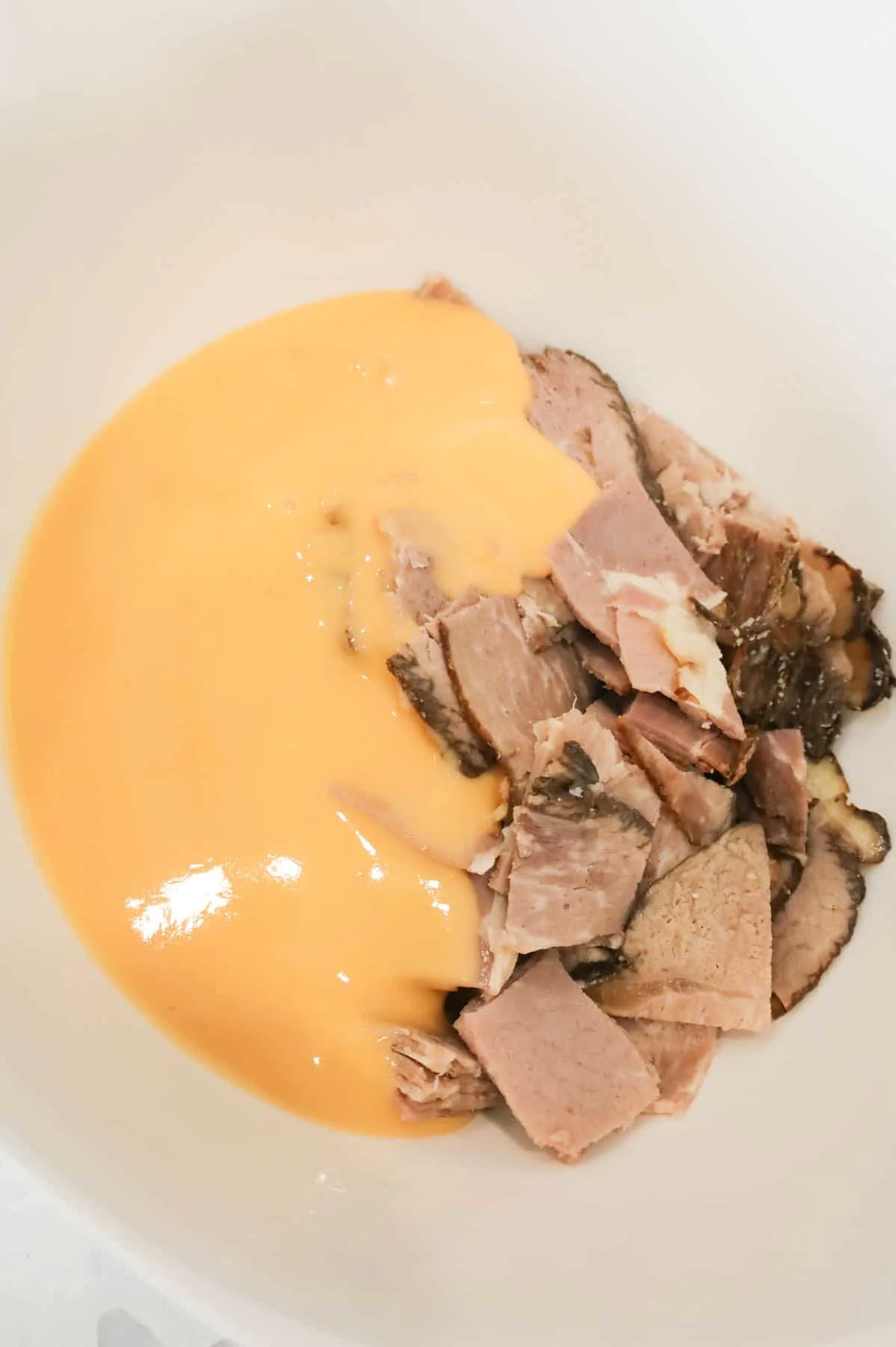 cheddar soup on top of roast beef in a mixing bowl