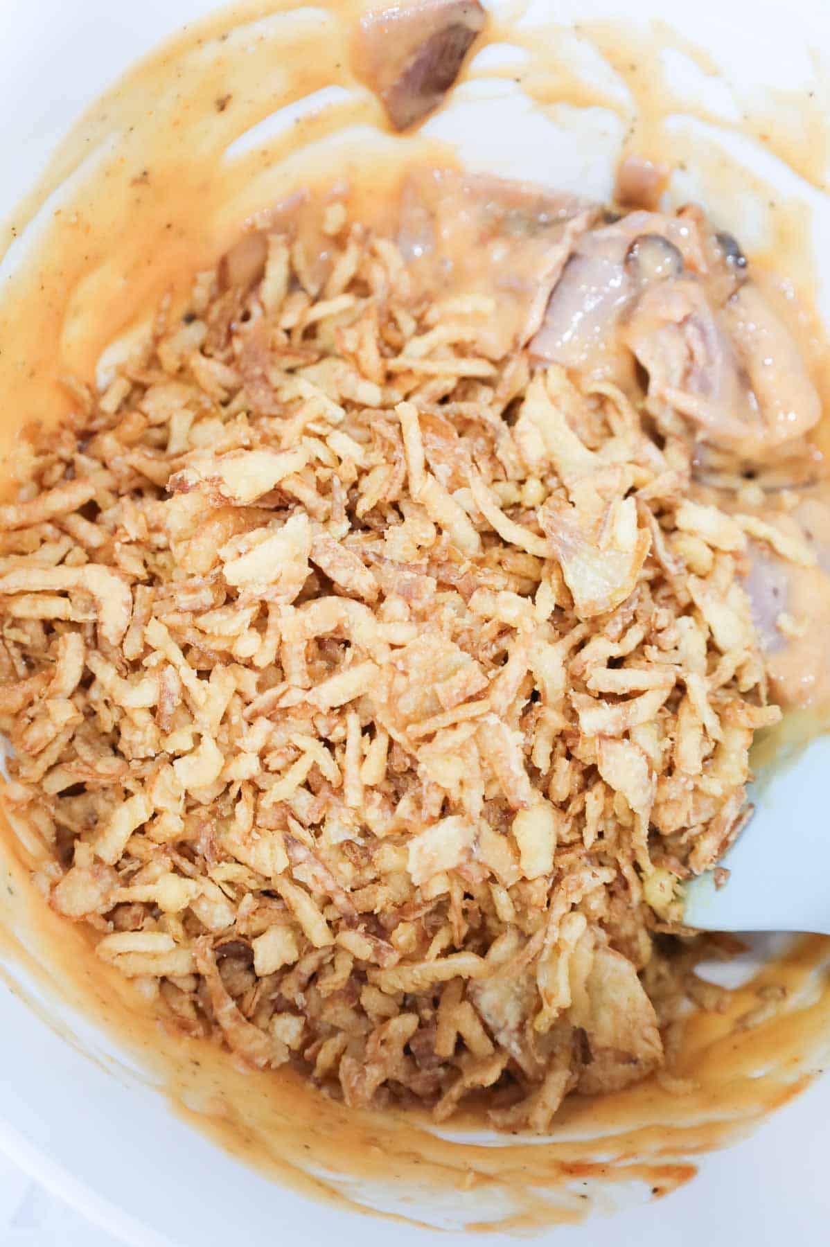 crispy fried onions on top of roast beef and cheddar soup mixture in a mixing bowl