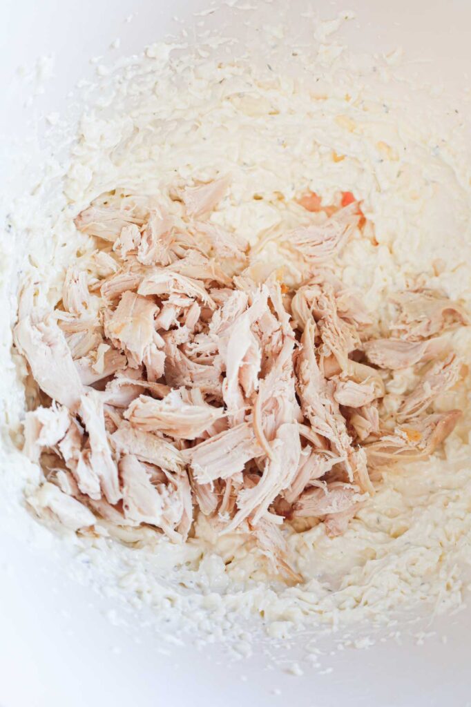 shredded chicken on top of cream cheese and ranch dressing mixture in a mixing bowl