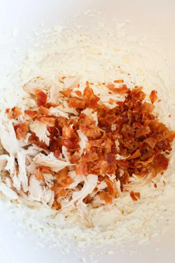 chopped bacon pieces on top of shredded chicken and cream cheese mixture in a mixing bowl