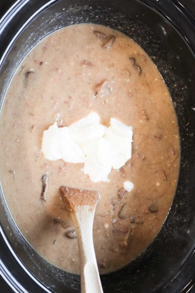 sour cream added to slow cooker with beef stroganoff