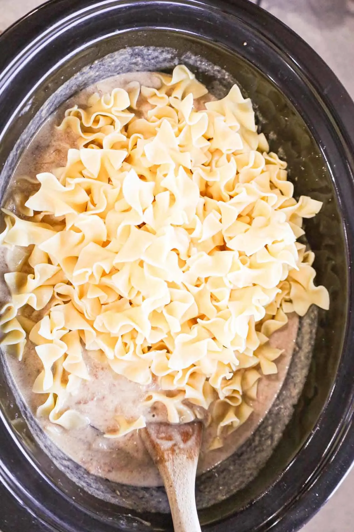 adding cooked egg noodles to slow cooker with beef stroganoff mixture